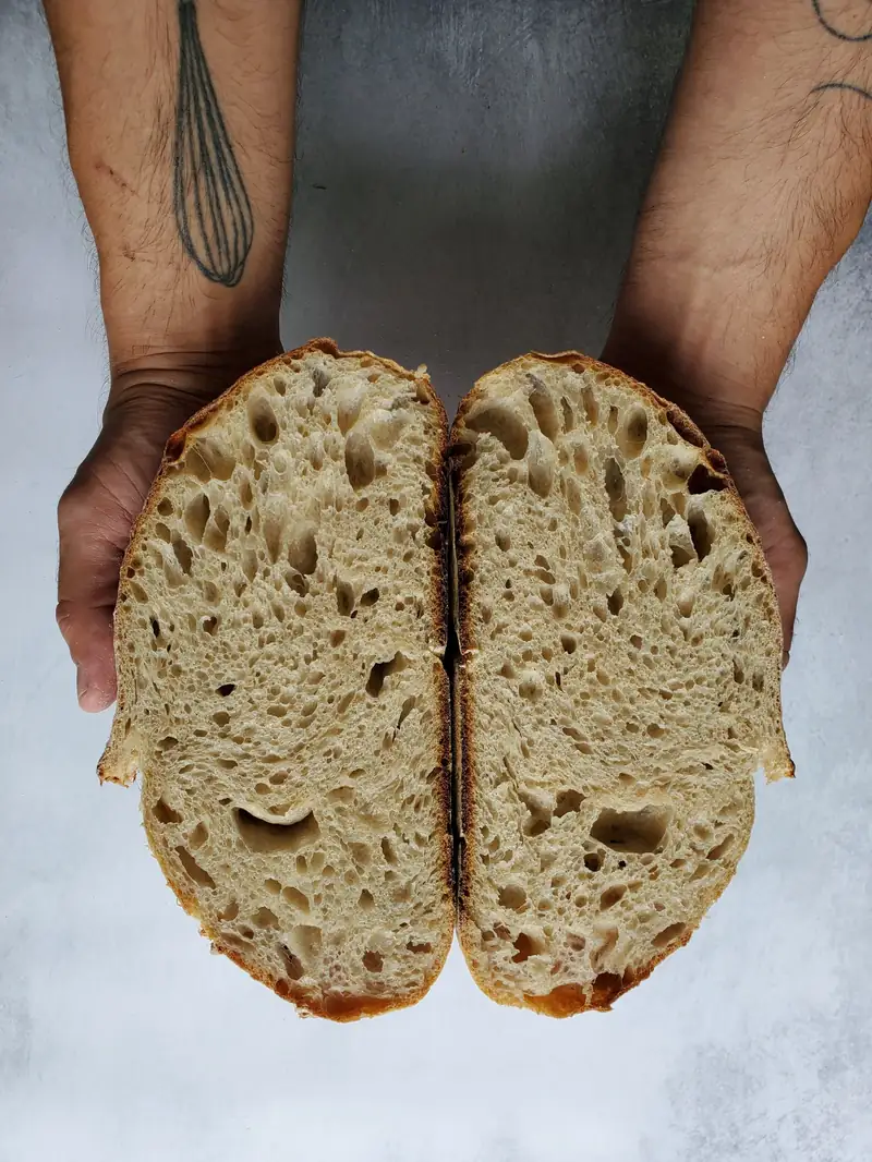 Baker's hands holding a freshly cut loaf of sourdough bread